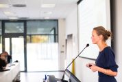 Junge Frau steht vor Seminarpublikum und spricht in ein Mikrofon lampenfieber